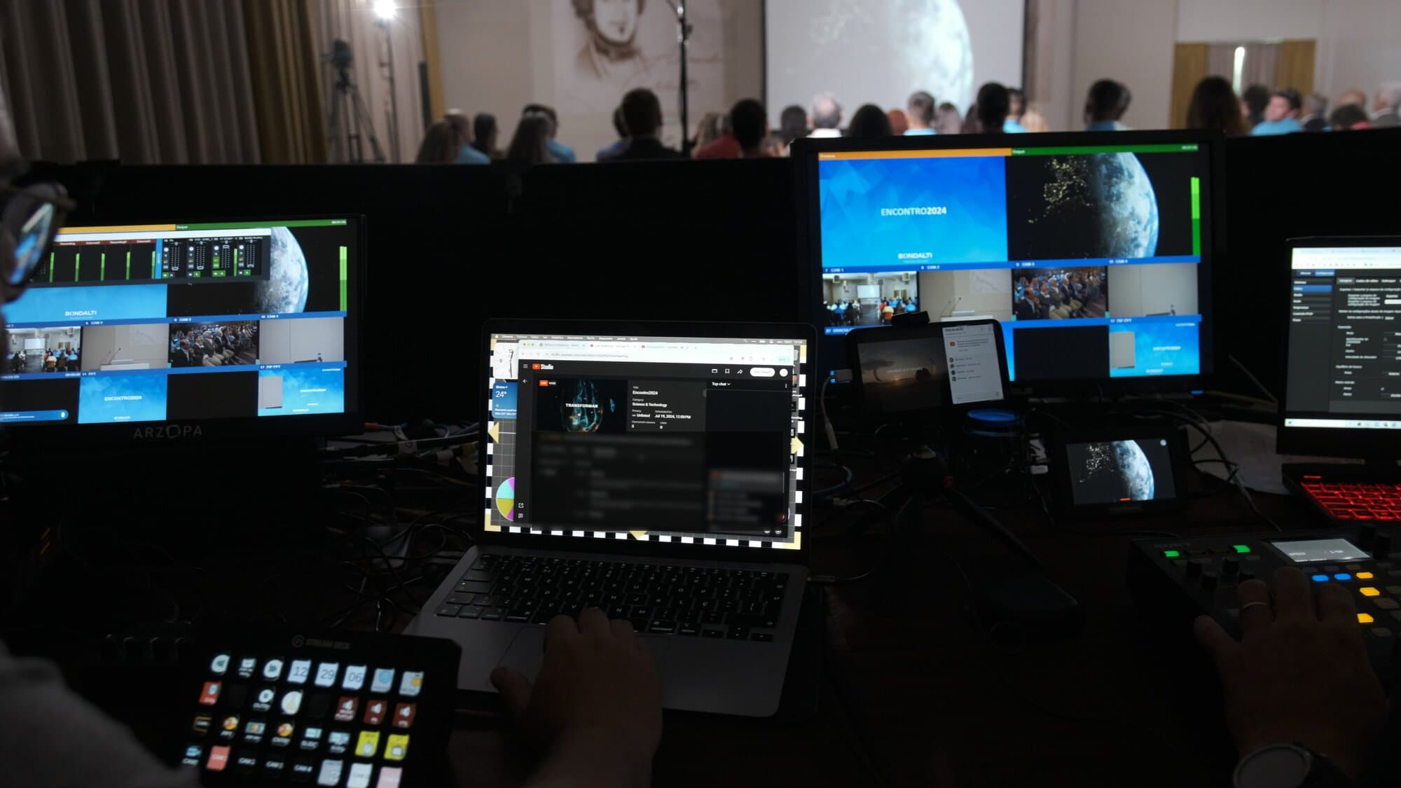 The control room at Bondalti's Encontro 2024, with the multiview, the Stream Deck and the camera controller in the foreground and the full room in the background, facing the screen