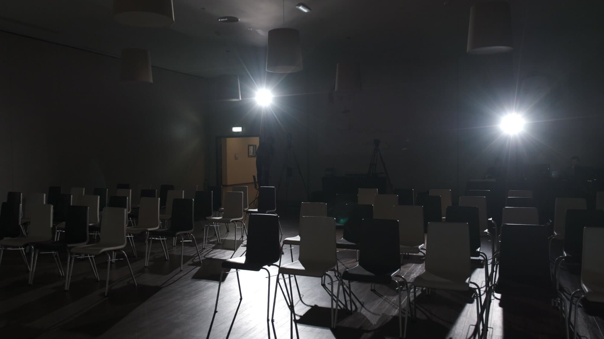 A sala às escuras, com as cadeiras vazias e dois projetores acesos ao fundo