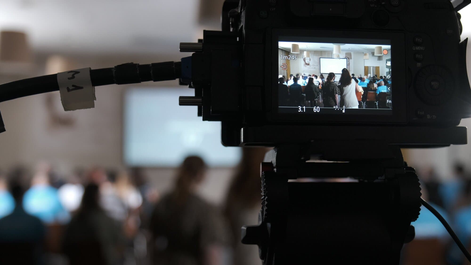 O visor de uma câmara GH5 em primeiro plano, a mostrar a sala cheia, com a plateia desfocada atrás