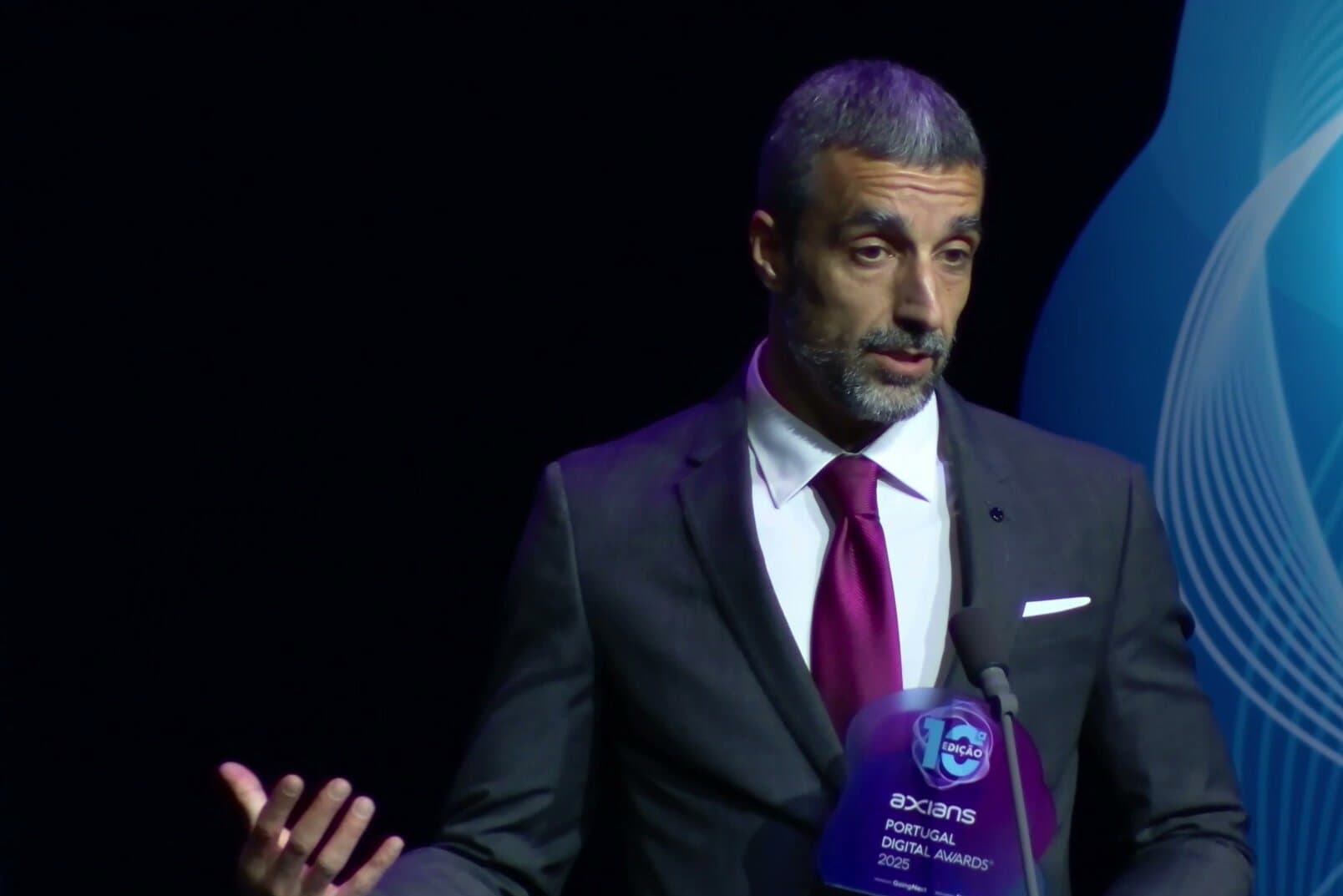 Um premiado ao microfone, com o troféu na mão, contra um fundo azul