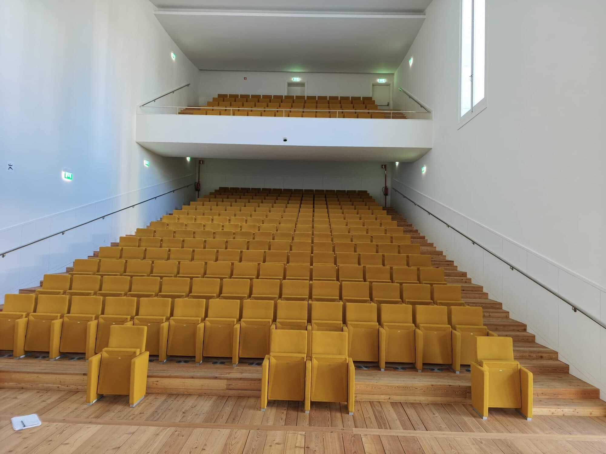 One of the audiences seen from the stage, with stepped yellow seats and the balcony above