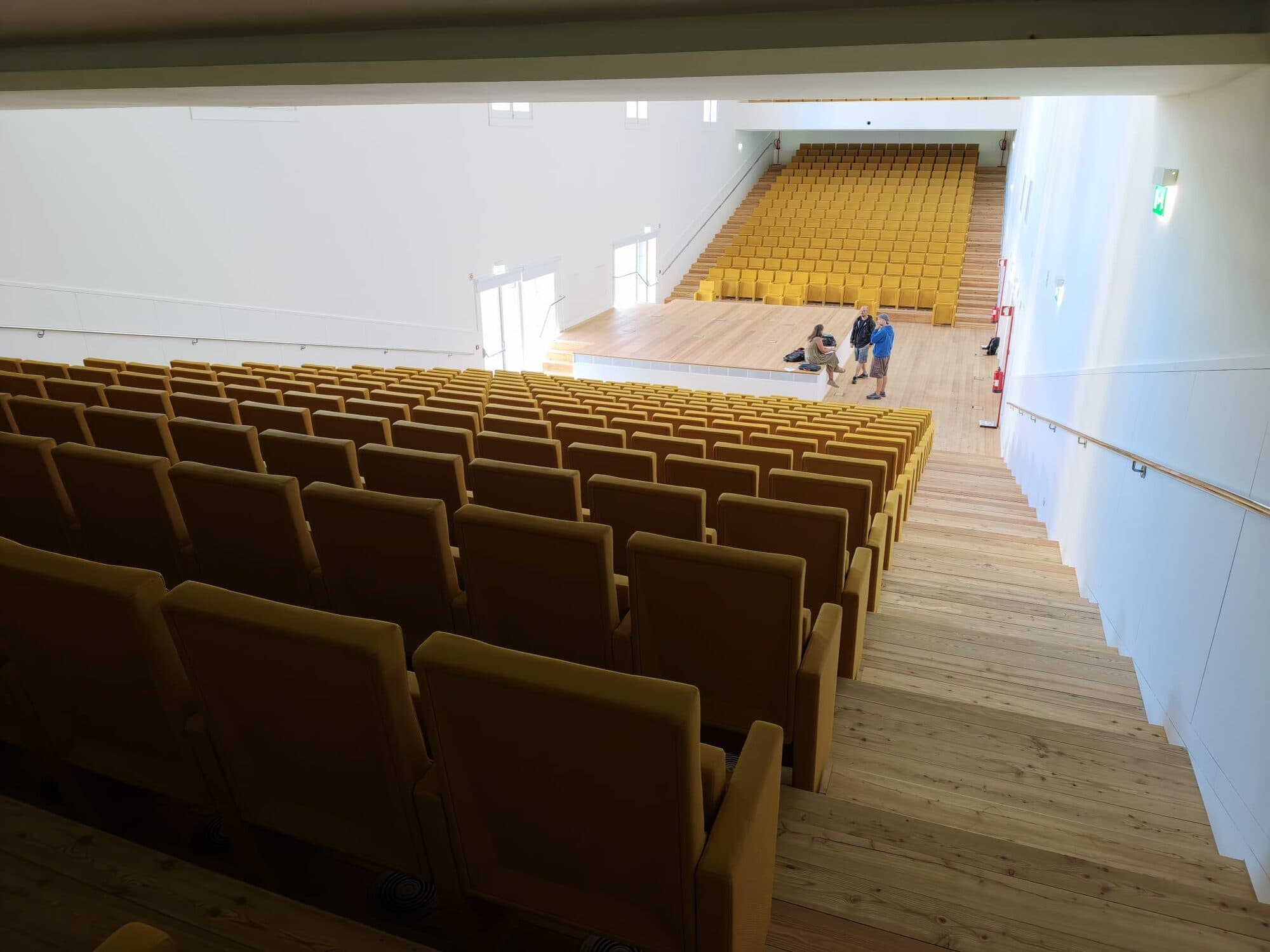 The Portugal Pavilion auditorium seen from the balcony, with the wooden stage in the middle and yellow seats on both sides