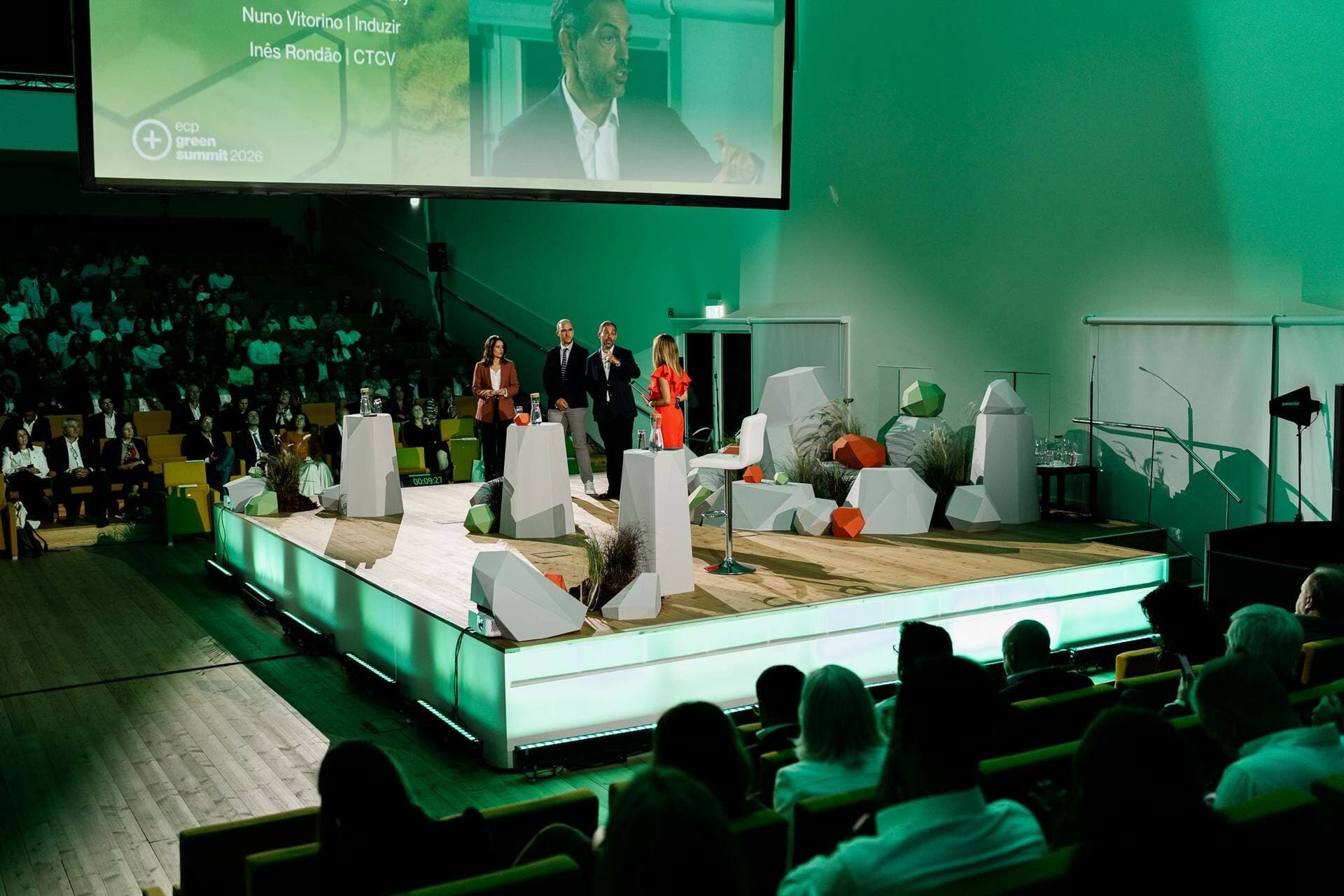 The auditorium on the day, with both audiences seated, a panel on stage and, on the screen above, a close-up of one of the speakers