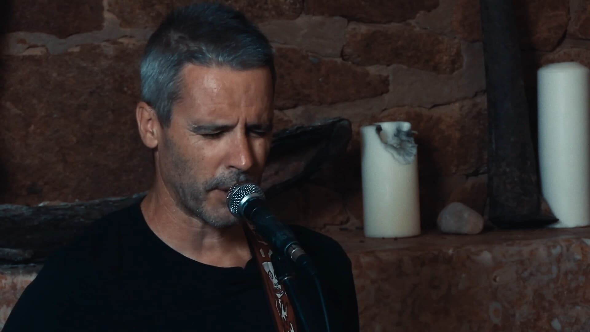 O João Leitão a cantar ao microfone diante da parede de pedra, no mesmo frame antes e depois do color grading